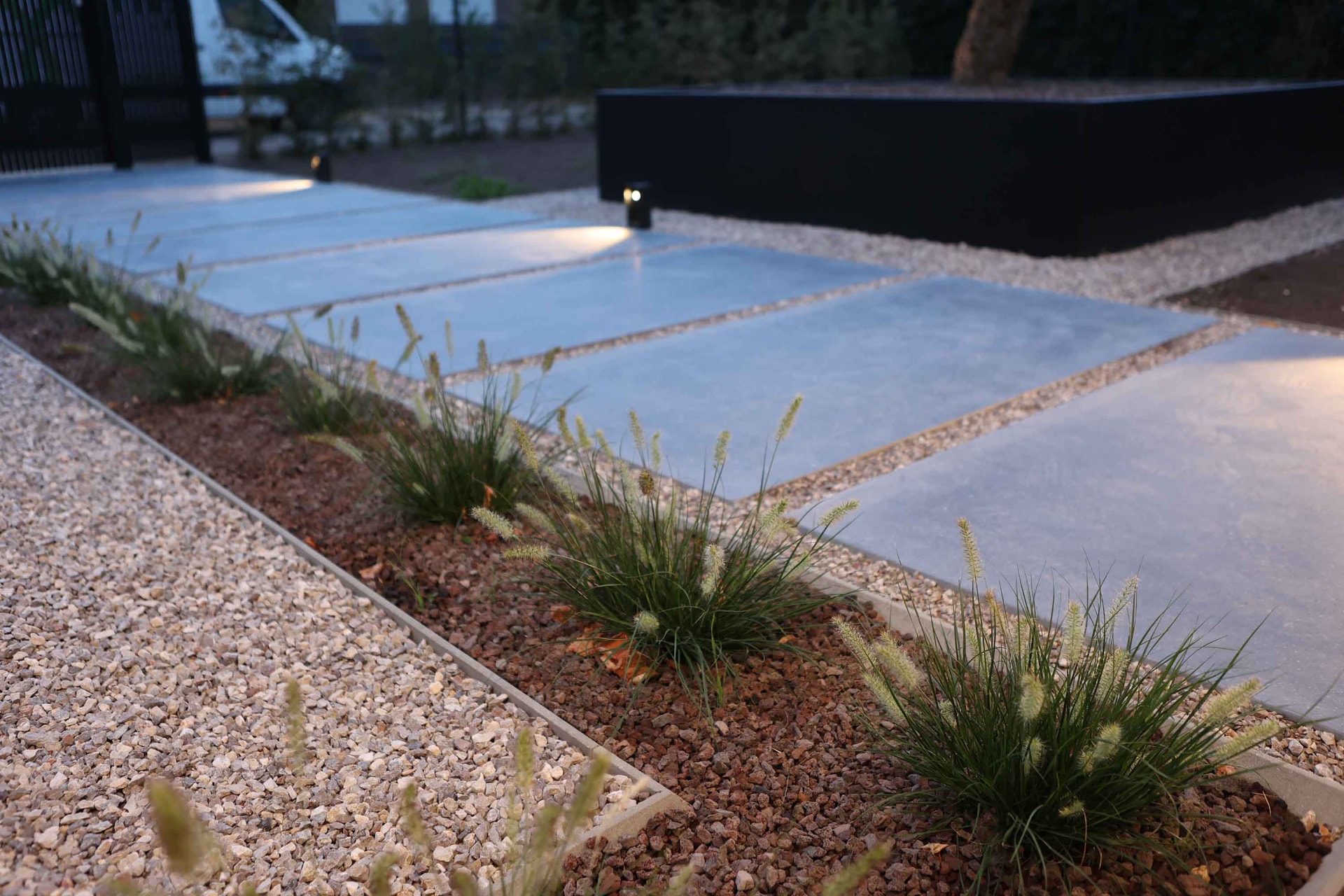 Verlichte tuinpad met betonklinkers en siergrassen bij avond